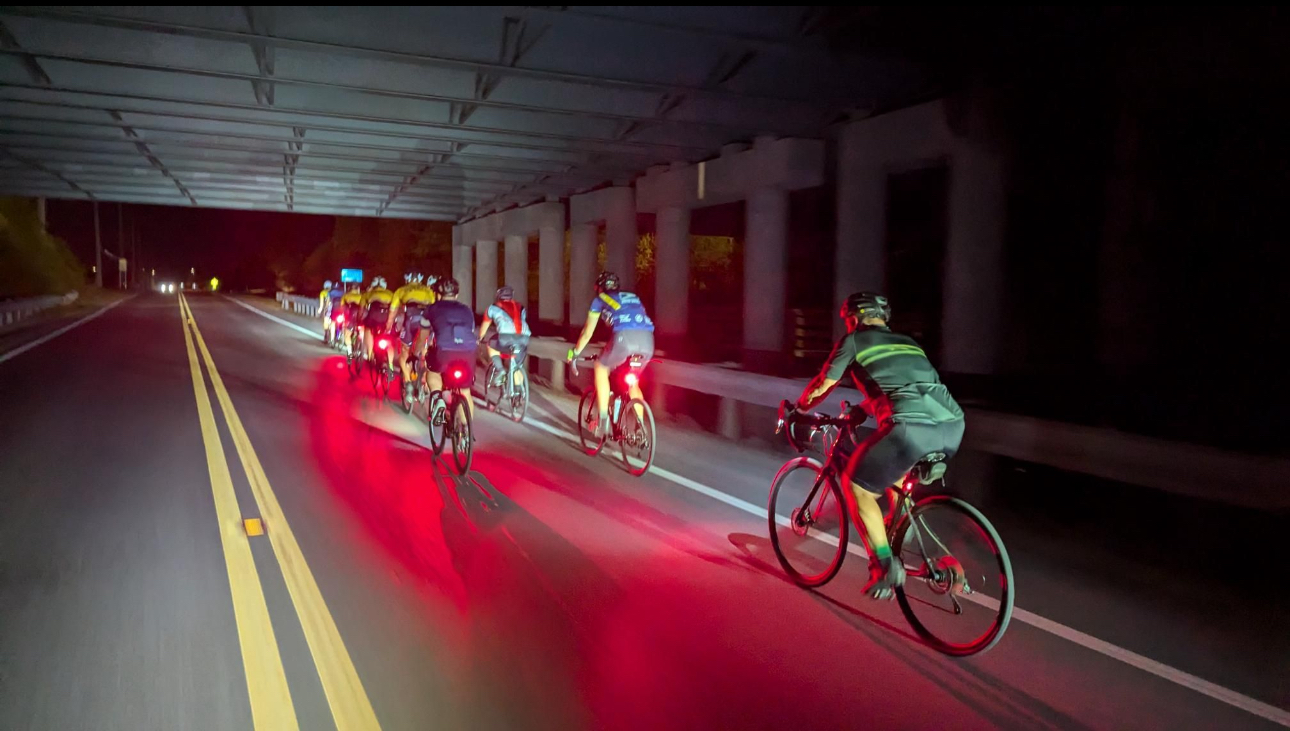 Cyclists riding under a bridge at night